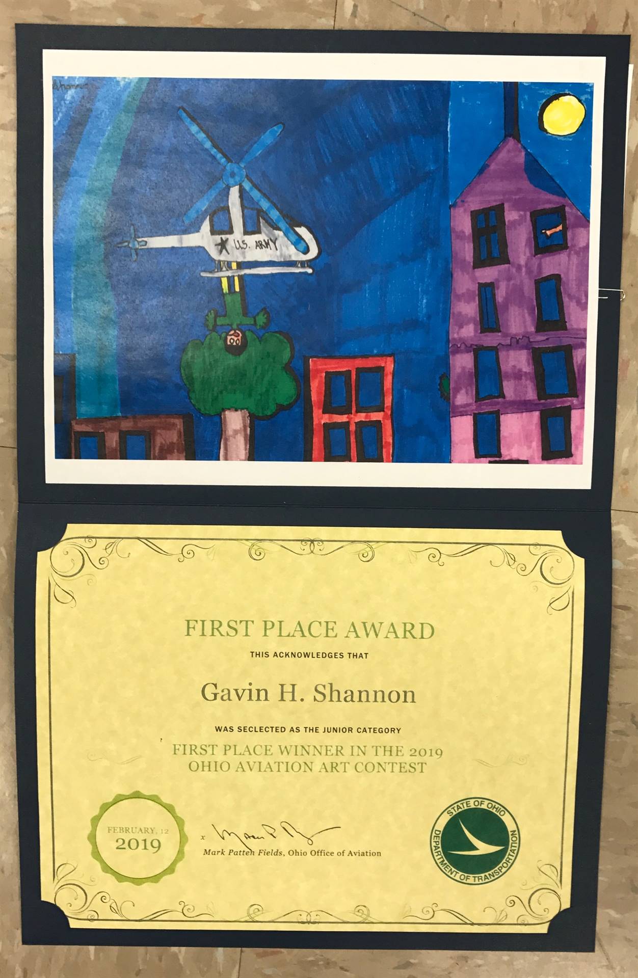 Student art display winner depicting US Army helicopter and houses.