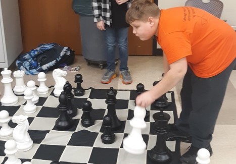 Middle School chess match being played on large floor chess board 