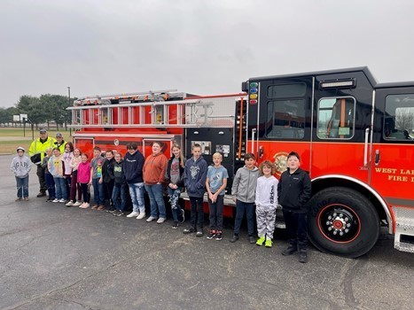 New West Lafayette orange and black fire engine truck with middle school students lined up beside it.
